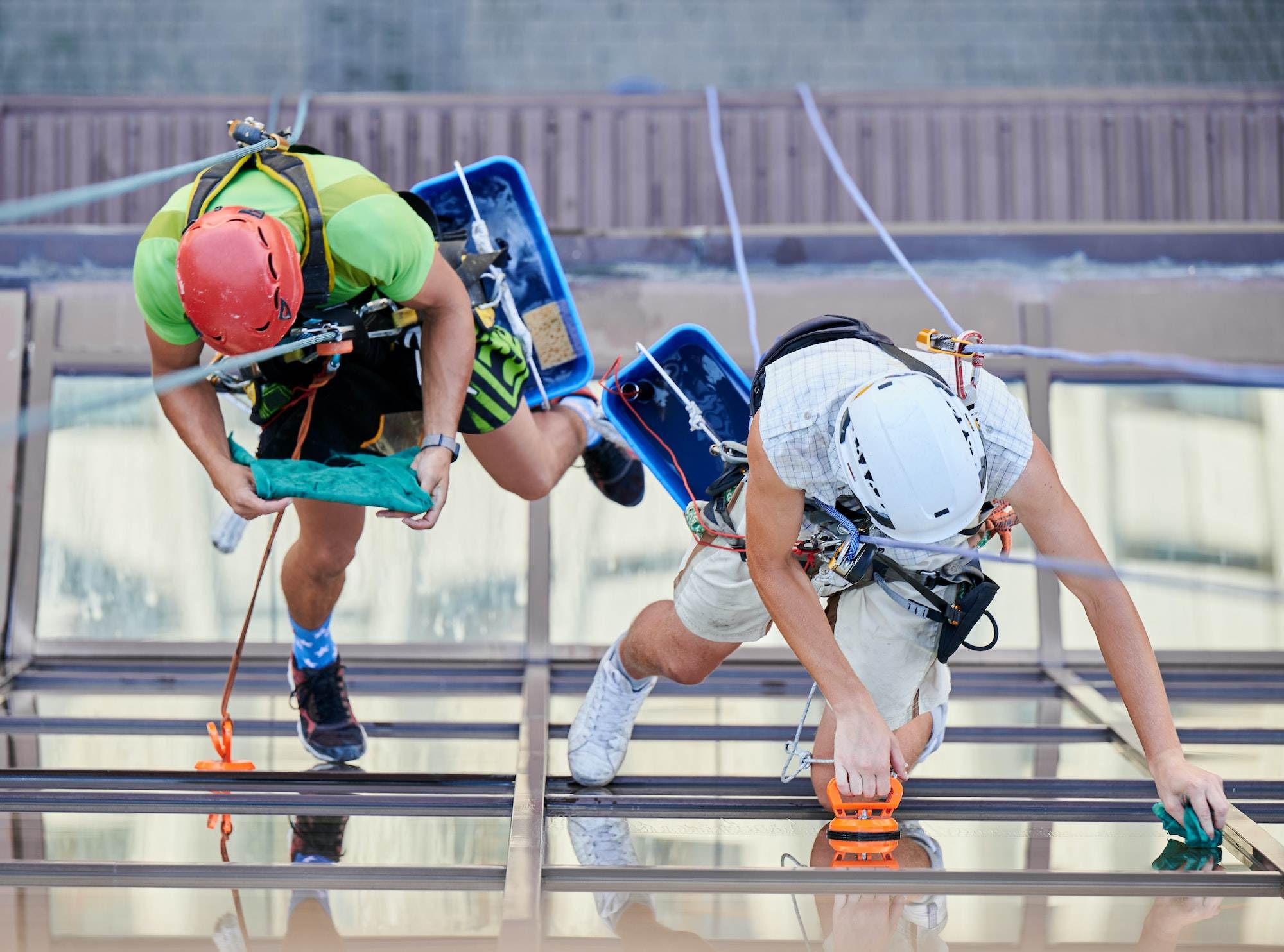 Industrial mountaineering worker cleaning window outside building.